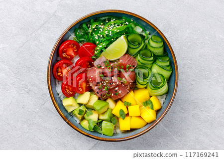 Healthy tuna poke bowl overhead top view. Poke is a traditional Hawaiian dish influenced by japanese and asian cuisine. Ahi poke is made of raw tuna chunks tossed over rice and topped with vegetables. Healthy tuna poke bowl overhead top view. Poke is a traditional Hawaiian dish influenced by japanese and asian cuisine. Ahi poke is made of raw tuna chunks tossed over rice and topped with vegetables. 117169241