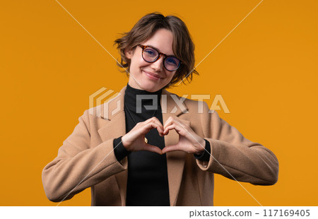 Smiling woman showing sign of shape heart. Positive lady on yellow. Love. Women health, volunteering, charity donation, gratitude symbol, flirting concept Smiling woman showing sign of shape heart. Positive lady on yellow. Love. Women health, volunteering, charity donation, gratitude symbol, flirting concept 117169405