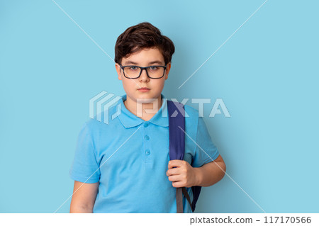 A schoolboy in glasses, with backpack, on blue background, look at camera 117170566