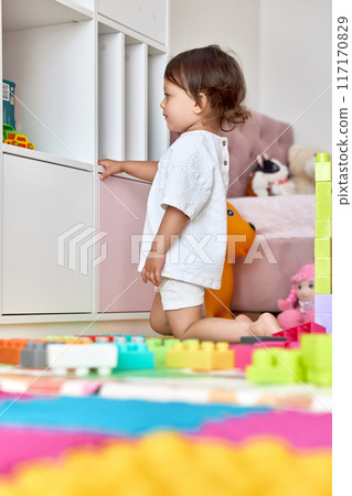 cute baby girl playing with colorful toys bricks in white bedroom 117170829