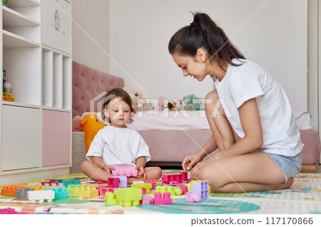cute baby girl and her loving mom playing with toy bricks in the children room, having fun together 117170866