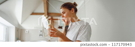 Smiling beautiful lady looking at her face in a small round mirror doing routine skincare procedures Smiling beautiful lady looking at her face in a small round mirror doing routine skincare procedures 117170943