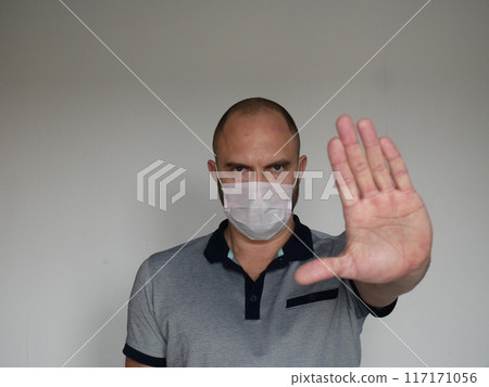 Stern looking man in medical mask shows open palm stop gesture on light background with copy space 117171056