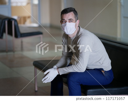 Man wearing protective gloves on hands and mask on face nervously impatiently waiting in the lobby 117171057