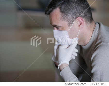 Man wearing protective gloves on hands and mask on face nervously impatiently waiting in the lobby 117171058