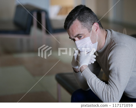 Man wearing protective gloves on hands and mask on face nervously impatiently waiting in the lobby 117171059