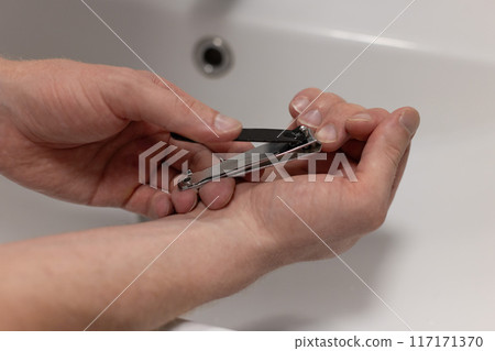 Closeup of a man cutting nails using nail clipper. Health care concept. Closeup of a man cutting nails using nail clipper. Health care concept. 117171370