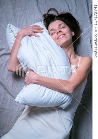 Girl hugs a white soft pillow and wants to sleep. Girl hugs a white soft pillow and wants to sleep. 117172741