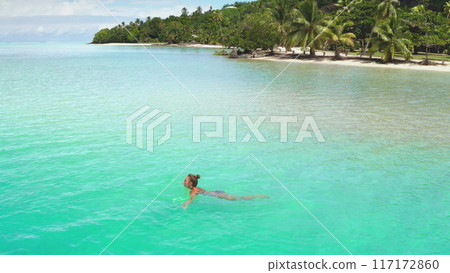 Young woman is swimming in the turquoise lagoon of maupiti island, french polynesia. The image is taken from a drone flying above the water Young woman is swimming in the turquoise lagoon of maupiti island, french polynesia. The image is taken from a drone flying above the water 117172860