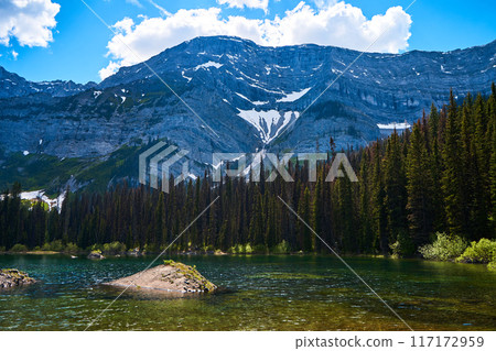 Incredibly beautiful transparent, emerald calm lake with reflection of rocky mountain on the Black Prince Cirque Trail. Majestic Canadian mountains with snow on sunny summer day in Alberta, Kananaskis 117172959