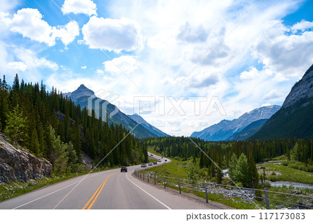 Beautiful view from a car on the Rocky Mountains in Banff National Park in Alberta. Panorama of a road in the mountains past a coniferous forest on a sunny day in summer. Beautiful view from a car on the Rocky Mountains in Banff National Park in Alberta. Panorama of a road in the mountains past a coniferous forest on a sunny day in summer. 117173083
