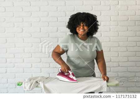 Young happy african american woman ironing clothes on ironing board at home. Copy space 117173132