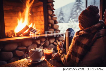 mug of coffee by the Christmas fireplace. Woman relaxes by warm fire with a cup of hot drink. Winter, Christmas holidays concept 117173267