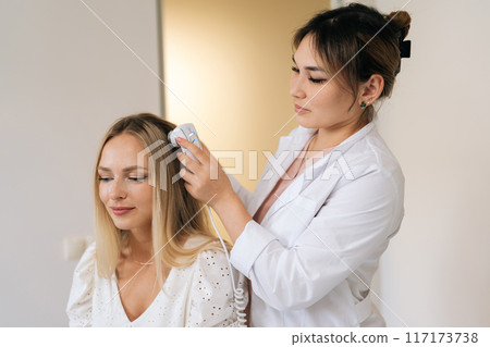 Concept of diagnostic complex for microscopic examination of hair and skin of scalp with trichoscope. Blonde female visiting dermatological clinic for examination of hair, scalp and hair follicles. Concept of diagnostic complex for microscopic examination of hair and skin of scalp with trichoscope. Blonde female visiting dermatological clinic for examination of hair, scalp and hair follicles. 117173738