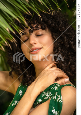 Cheerful woman with dark curls among tropical leaves 117173746