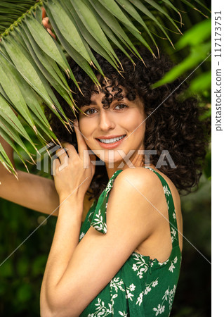 Woman with dark curly hair among fresh greenery in atmosphere of natural coziness Woman with dark curly hair among fresh greenery in atmosphere of natural coziness 117173751
