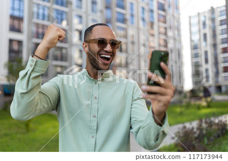Man scrolling online using cellphone reading news in internet walking on big city urban street outside Man scrolling online using cellphone reading news in internet walking on big city urban street outside 117173944