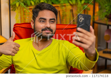 Happy Indian man taking selfie on smartphone communicating video call home online with subscribers 117174118