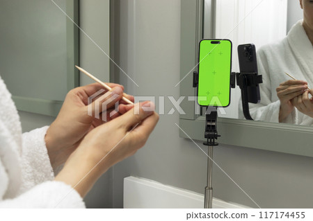 Mockup White Woman Makes Manicure At Home. Female Holds Wooden Cuticle Pusher Stick And Green Chroma Key Screen On Device, E-learning, Online Education, Personal Hygiene. Horizontal 117174455