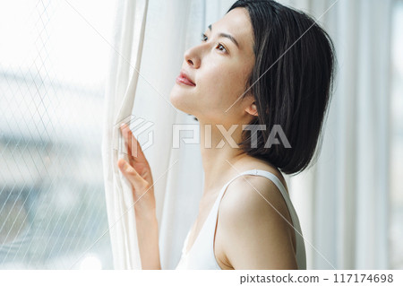 A woman opening the curtains at the window in the morning 117174698