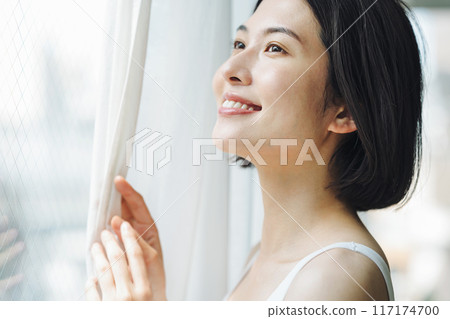 一個女人早上打開窗邊的窗簾 一個女人早上打開窗邊的窗簾 117174700