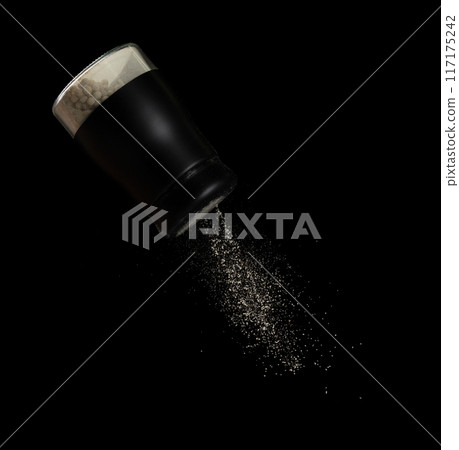 Pepper seed seasoning powder flavor falling from shaker bottle, ground pepper and seasoning powder splash in mid air. Seasoning powder shaker spice up taste of food over black background isolated 117175242
