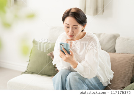 A middle woman looking at a smartphone in the living room 117176375