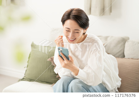 A middle woman looking at a smartphone in the living room A middle woman looking at a smartphone in the living room 117176376