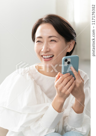 A middle woman looking at a smartphone in the living room 117176382