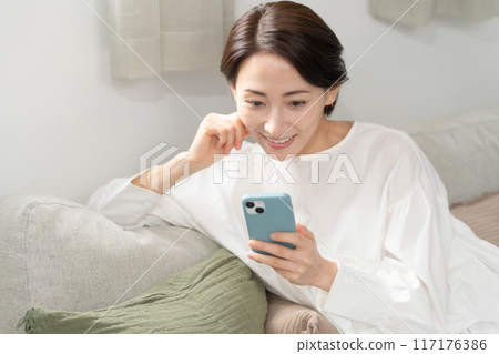 A middle woman looking at a smartphone in the living room A middle woman looking at a smartphone in the living room 117176386