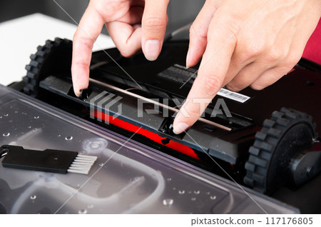 Close-up of a young Caucasian woman's hands servicing the brush compartment of a robot vacuum cleaner. Automated home cleaning systems 117176805