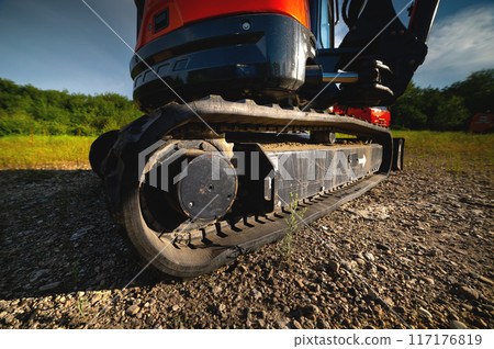 Close-up of rubber tracks of a small excavator outdoors surrounded by grass and greenery on a sunny day Close-up of rubber tracks of a small excavator outdoors surrounded by grass and greenery on a sunny day 117176819