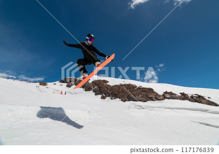 A young woman in a helmet makes a ski jump high in the mountains. Winter sport. Snowboarder woman doing a trick 117176839