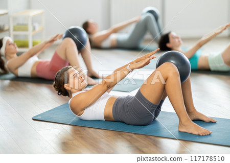 Young girl doing press with softball band between legs lying on the floor 117178510