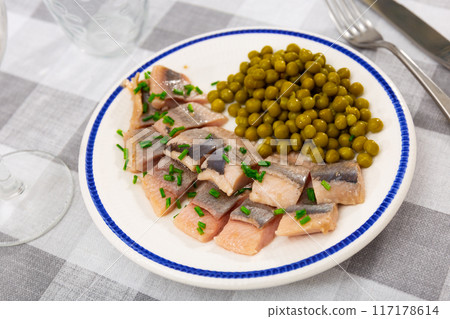 Tasty slices herring fillet with canned green peas served on plate 117178614
