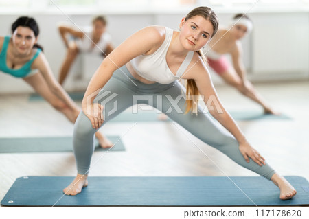 Young woman during Pilates strength training standing performs exercises Young woman during Pilates strength training standing performs exercises 117178620