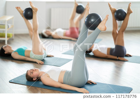 Young girl doing exercises holding softball between feet Young girl doing exercises holding softball between feet 117178776