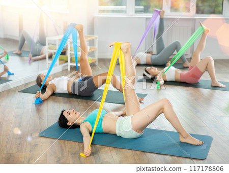 Girl lying and perform variety of exercises to strengthen muscles of press with wide resistance band 117178806