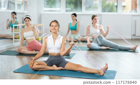 Young girls doing arm workout with band sitting leg extended Young girls doing arm workout with band sitting leg extended 117178840