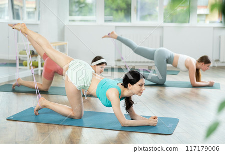 Young girls practicing back leg lift with band standing on knees 117179006