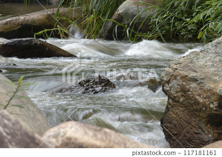Crystal-clear waterfall dances over smooth stones, weaving a vibrant tapestry through lush green nature Crystal-clear waterfall dances over smooth stones, weaving a vibrant tapestry through lush green nature 117181161