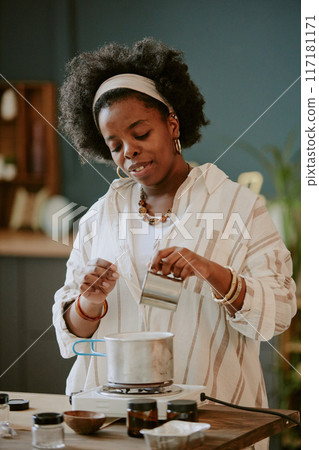 Black woman in striped shirt engaging in making a milk-based beverage in a warmly lit kitchen with various spices around, capturing a moment of culinary activity Black woman in striped shirt engaging in making a milk-based beverage in a warmly lit kitchen with various spices around, capturing a moment of culinary activity 117181171