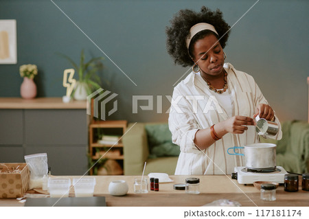 Young African American woman concentrating on ingredients while cooking in modern kitchen setting with various utensils on counter Young African American woman concentrating on ingredients while cooking in modern kitchen setting with various utensils on counter 117181174