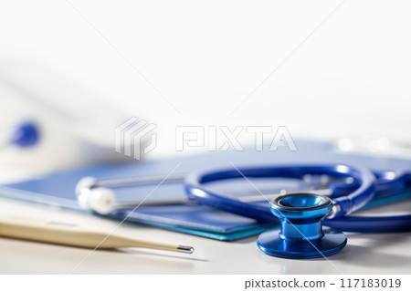 A stethoscope, a thermometer, and a medical record on a table. Medical image A stethoscope, a thermometer, and a medical record on a table. Medical image 117183019