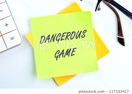 Text Dangerous game on a sticker in a composition with a calculator and glasses on top on a white background Text Dangerous game on a sticker in a composition with a calculator and glasses on top on a white background 117183427