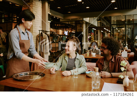 Server bringing dishes to smiling couple at cozy restaurant, creating warm atmosphere. Diverse group enjoying meal surrounded by modern and inviting interior Server bringing dishes to smiling couple at cozy restaurant, creating warm atmosphere. Diverse group enjoying meal surrounded by modern and inviting interior 117184261