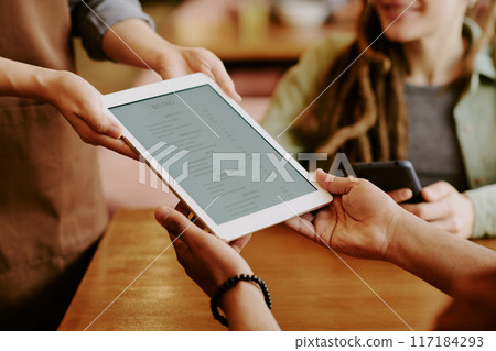 Digital menu handed over at casual restaurant table, illustrating modern dining experience Work and social interaction visible in relaxed environment 117184293