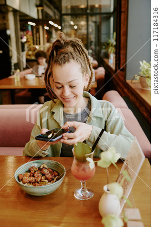 Individual photographing delicious meal in cozy restaurant setting, complementing it with refreshing drink, exuding sense of leisure and enjoyment 117184316