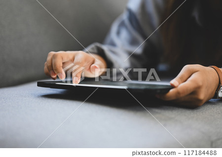 Close up image of unrecognizable woman hands using digital tablet, lying on couch at home 117184488
