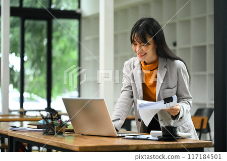 Asian female financier worker using laptop and checking statistic report at office desk 117184501